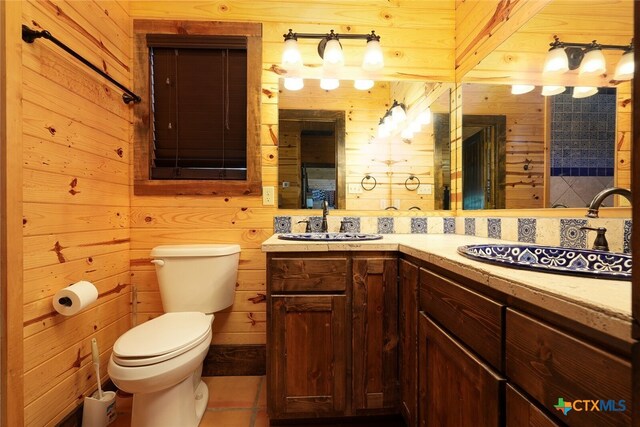 bathroom featuring toilet, vanity, wooden walls, and tile patterned floors