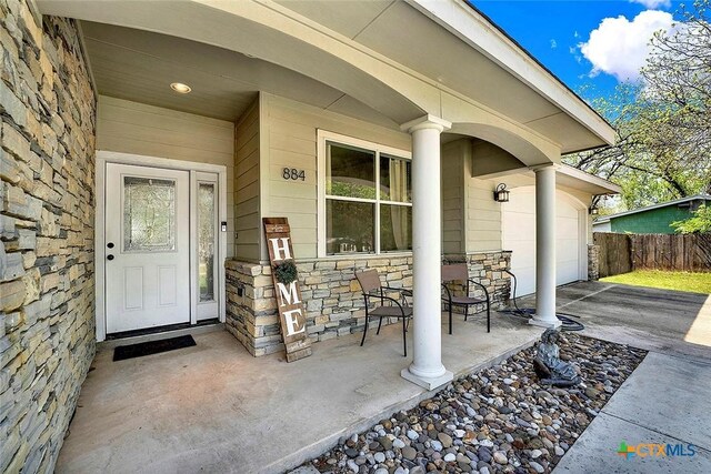 doorway to property with fence, a porch, stone siding, and driveway