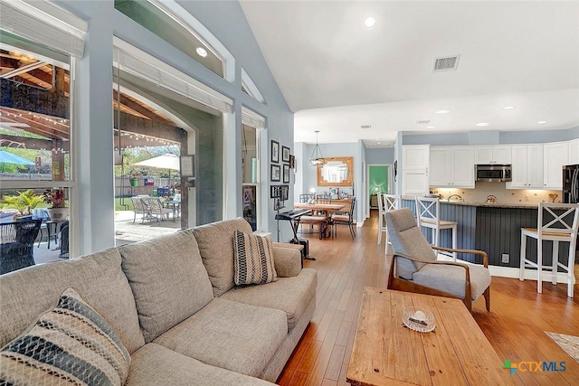 living area with lofted ceiling, visible vents, recessed lighting, and light wood-type flooring