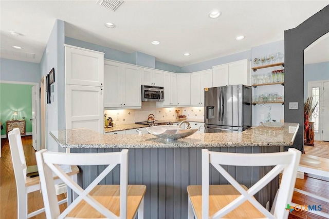 kitchen featuring white cabinets, visible vents, light stone counters, a breakfast bar, and appliances with stainless steel finishes