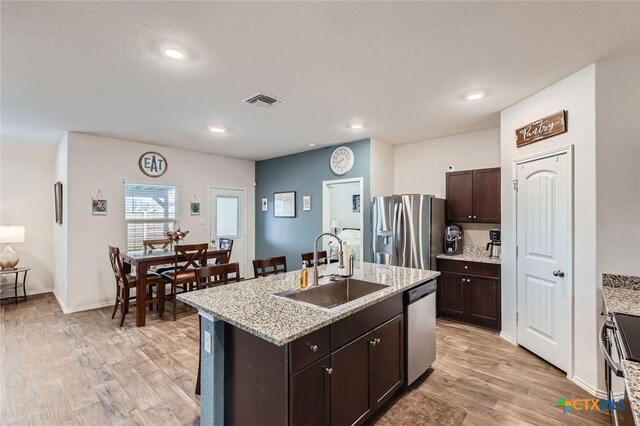 kitchen featuring a sink, dark brown cabinetry, light wood-type flooring, stainless steel appliances, and a kitchen island with sink