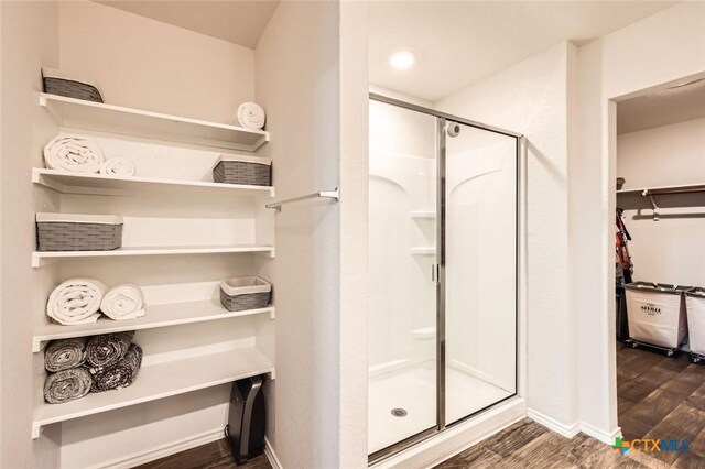 bathroom featuring a walk in closet, wood finished floors, a stall shower, and baseboards