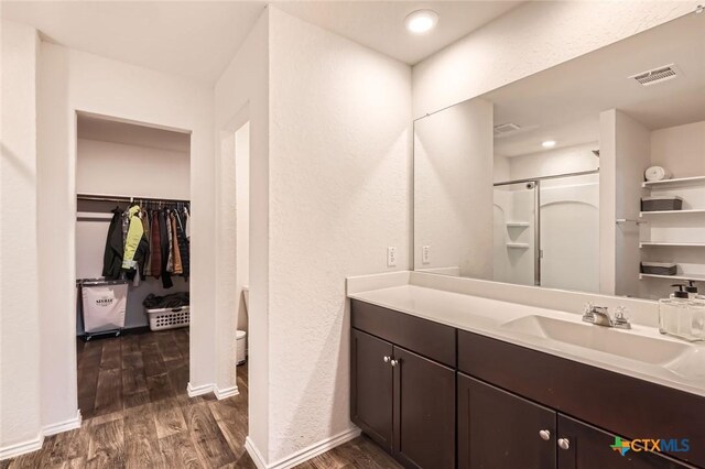 bathroom featuring visible vents, wood finished floors, a shower stall, baseboards, and vanity