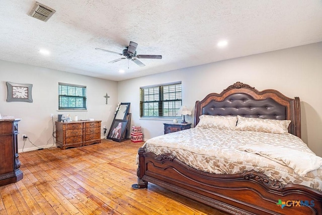 bedroom featuring ceiling fan, a textured ceiling, multiple windows, and light wood-type flooring