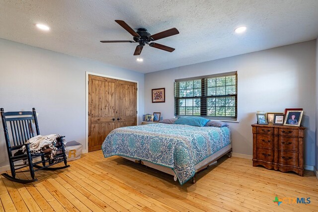 bedroom with ceiling fan, a closet, a textured ceiling, and light wood-type flooring