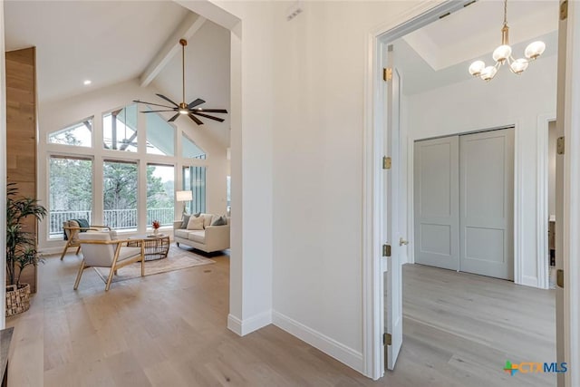 interior space with beamed ceiling, ceiling fan with notable chandelier, high vaulted ceiling, and light hardwood / wood-style flooring