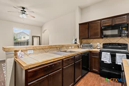 kitchen featuring light hardwood / wood-style floors, sink, black appliances, kitchen peninsula, and backsplash