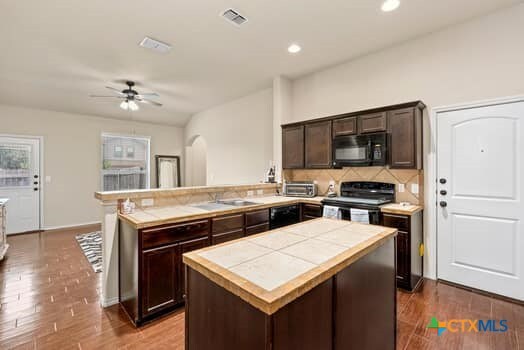 kitchen featuring black appliances, wood-type flooring, a kitchen island, dark brown cabinets, and kitchen peninsula