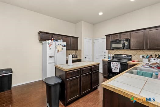 kitchen with dark brown cabinets, black appliances, dark hardwood / wood-style flooring, and tasteful backsplash