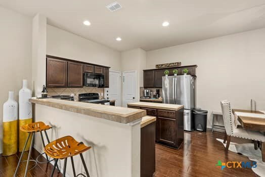 kitchen featuring dark brown cabinetry, black appliances, kitchen peninsula, tasteful backsplash, and dark hardwood / wood-style flooring