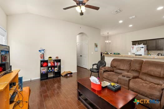 living room featuring ceiling fan with notable chandelier, dark hardwood / wood-style flooring, and vaulted ceiling