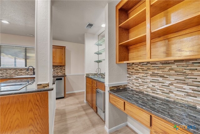 kitchen with stainless steel dishwasher, dark stone counters, sink, and decorative backsplash