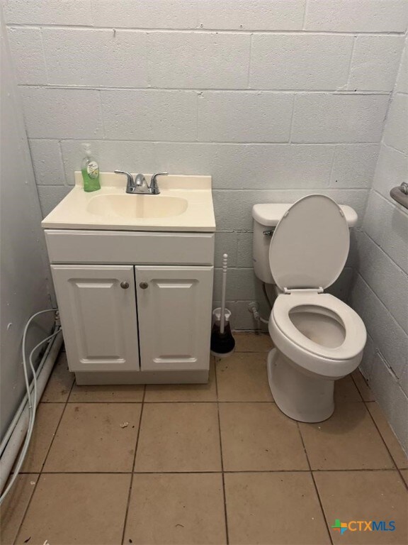 half bathroom with vanity, toilet, concrete block wall, and tile patterned floors
