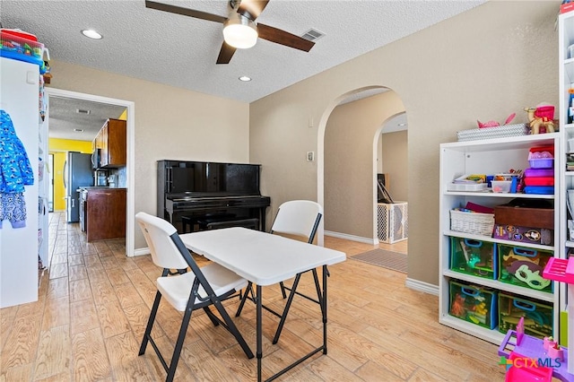 office area featuring arched walkways, visible vents, light wood finished floors, and a textured ceiling