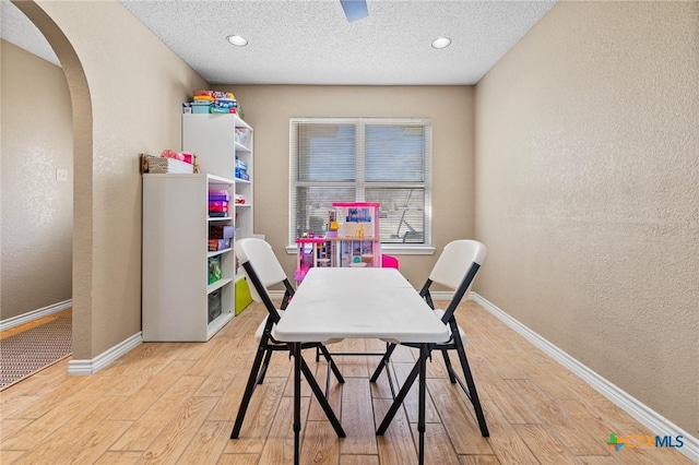 dining room with baseboards, light wood-style flooring, a textured wall, arched walkways, and a textured ceiling