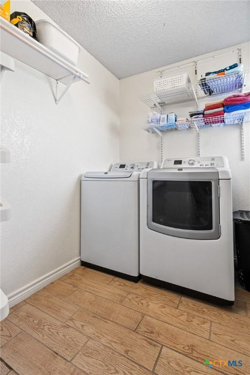 washroom with independent washer and dryer, a textured ceiling, light wood finished floors, baseboards, and laundry area