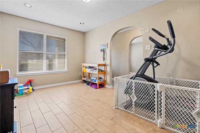 game room with baseboards, a textured ceiling, wood finished floors, and arched walkways