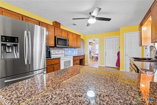 kitchen with a sink, stainless steel appliances, brown cabinetry, and decorative backsplash