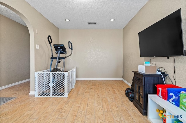 workout room featuring arched walkways, visible vents, light wood-type flooring, and baseboards