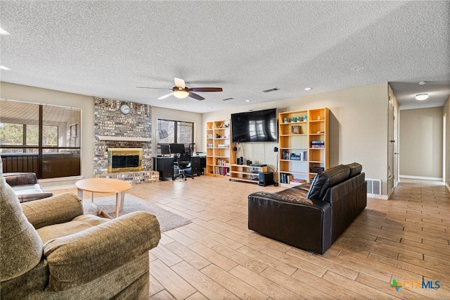 living area featuring visible vents, a ceiling fan, a textured ceiling, a fireplace, and light wood finished floors