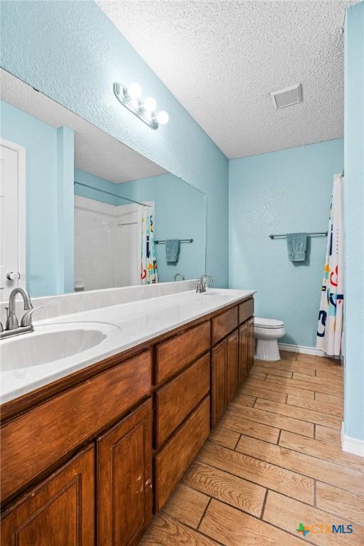 full bath featuring wood finish floors, double vanity, a sink, a textured ceiling, and toilet