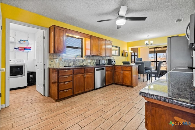 kitchen featuring a peninsula, stainless steel appliances, brown cabinetry, washer / clothes dryer, and a sink