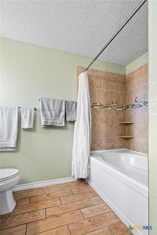 full bathroom featuring baseboards, wood finish floors, shower / tub combo, a textured ceiling, and toilet