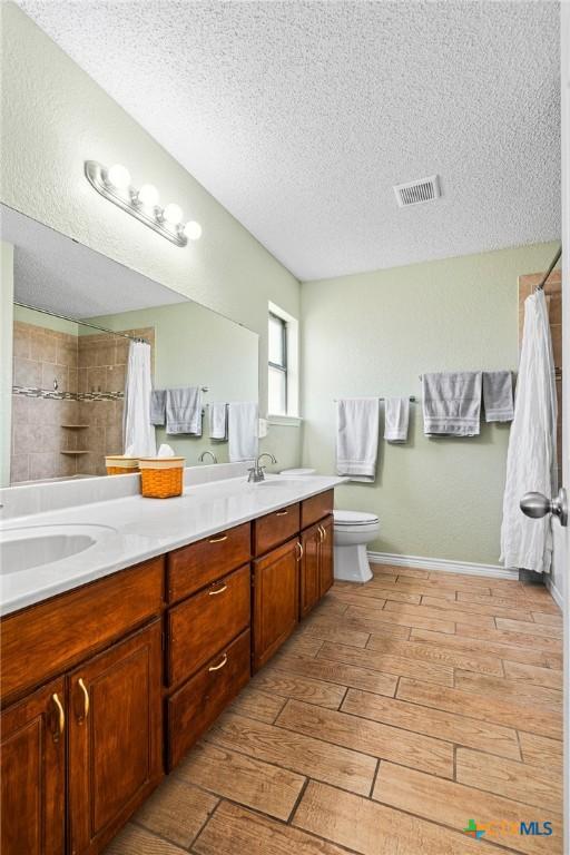 bathroom featuring visible vents, a textured ceiling, a shower with shower curtain, double vanity, and wood tiled floor