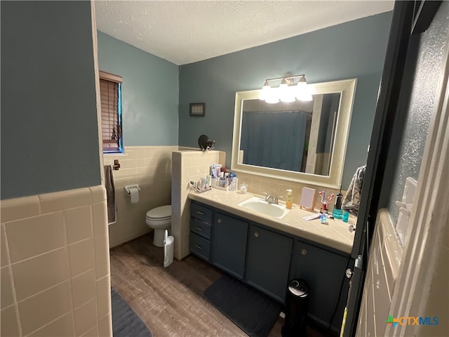 bathroom featuring a textured ceiling, hardwood / wood-style floors, vanity, toilet, and tile walls