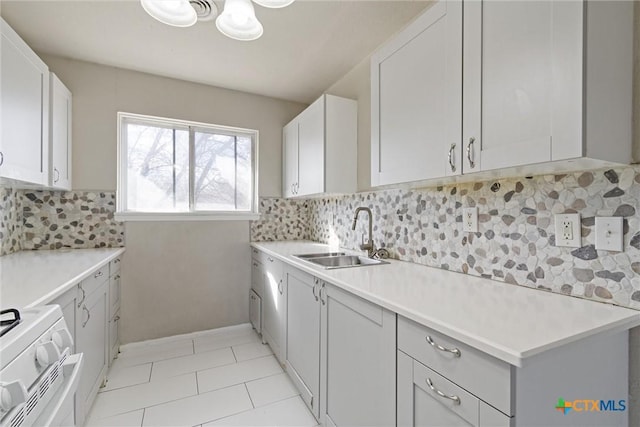 kitchen with light tile patterned floors, white range with gas stovetop, a sink, light countertops, and backsplash