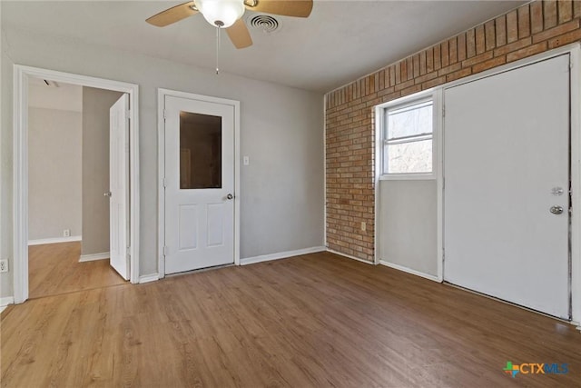 entryway featuring a ceiling fan, visible vents, brick wall, light wood finished floors, and baseboards