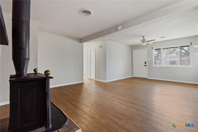 living room with visible vents, baseboards, wood finished floors, and a wood stove