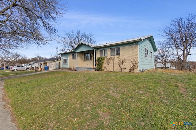 view of front of house with metal roof, driveway, brick siding, and a front yard