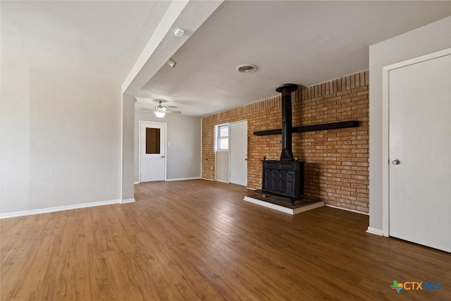 unfurnished living room featuring visible vents, a ceiling fan, wood finished floors, baseboards, and a wood stove