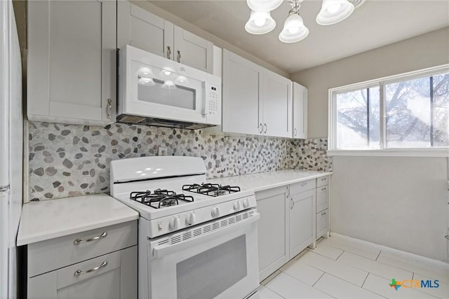 kitchen featuring tasteful backsplash, light countertops, gray cabinets, an inviting chandelier, and white appliances