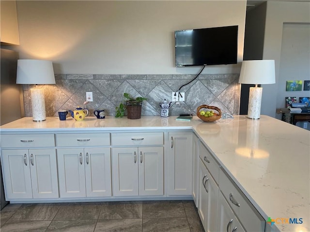 kitchen with tasteful backsplash, light stone countertops, and white cabinets