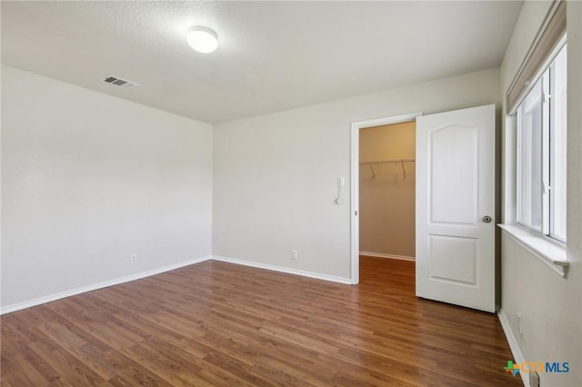 unfurnished bedroom featuring wood finished floors, baseboards, a spacious closet, and a closet