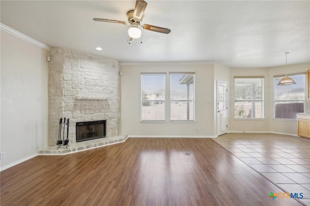 unfurnished living room with ceiling fan, ornamental molding, a fireplace, wood finished floors, and baseboards