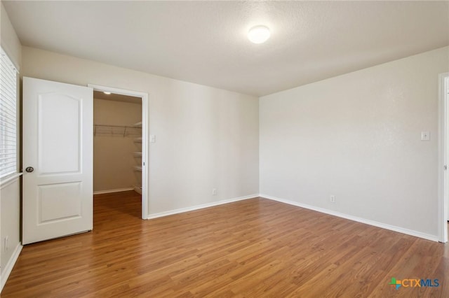 unfurnished bedroom with light wood-style flooring, a walk in closet, and baseboards