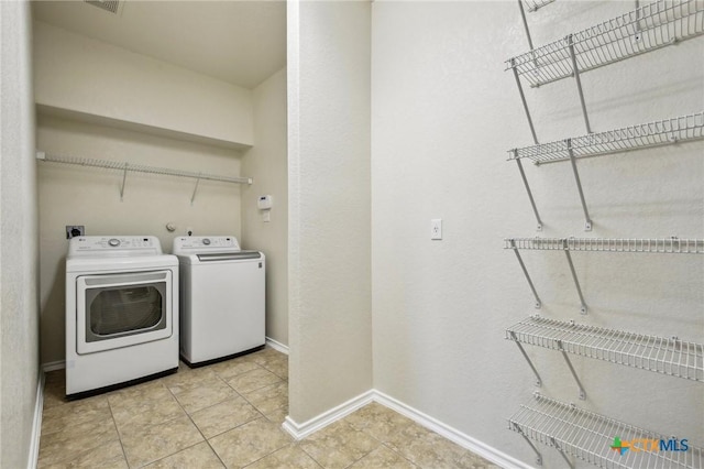clothes washing area featuring separate washer and dryer, baseboards, and light tile patterned floors