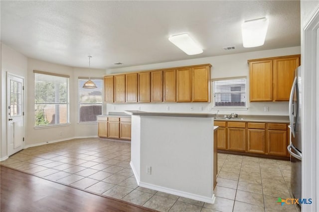 kitchen featuring a sink, light countertops, light tile patterned floors, freestanding refrigerator, and decorative light fixtures