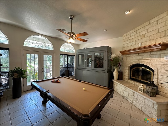 recreation room featuring ceiling fan, a textured ceiling, light tile patterned floors, a stone fireplace, and billiards