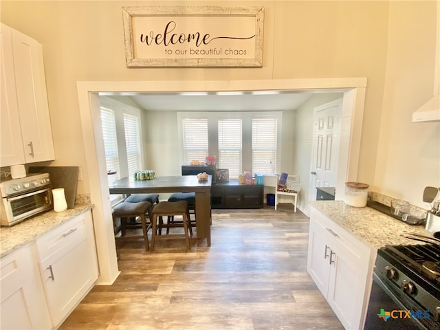 kitchen featuring gas range oven, white cabinetry, and light stone countertops