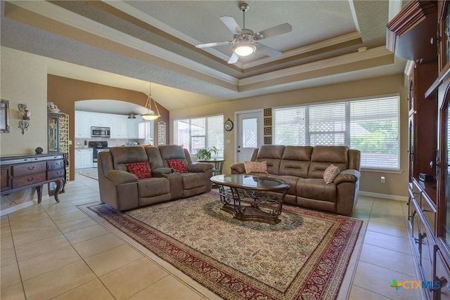 living room with plenty of natural light, a ceiling fan, a tray ceiling, and light tile patterned flooring