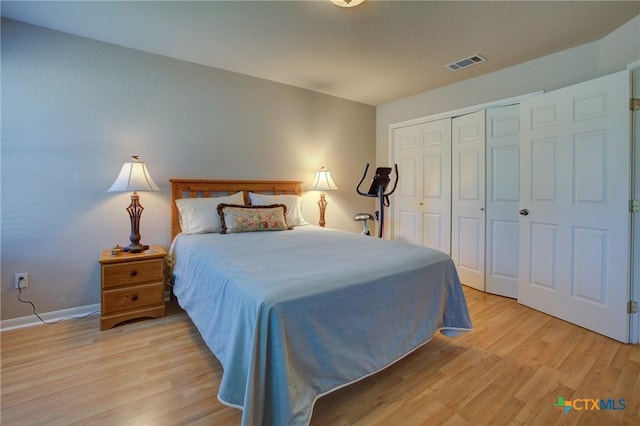 bedroom with baseboards, light wood finished floors, visible vents, and a closet