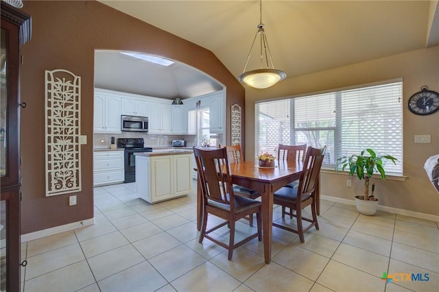 dining area with light tile patterned flooring, vaulted ceiling, arched walkways, and baseboards