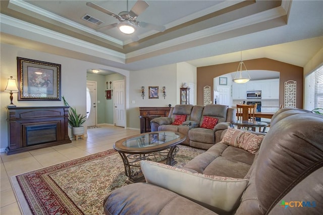 living room featuring a tray ceiling, visible vents, a ceiling fan, light tile patterned floors, and arched walkways