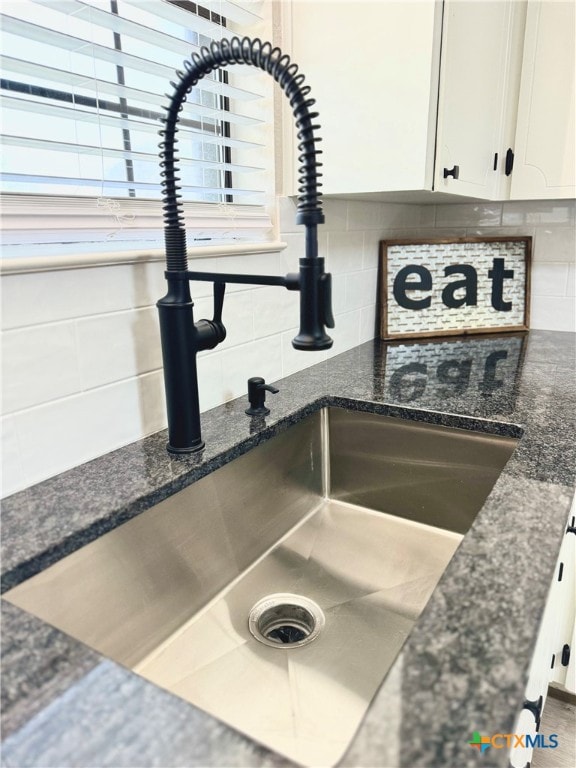 interior details with dark stone counters, tasteful backsplash, sink, and white cabinets