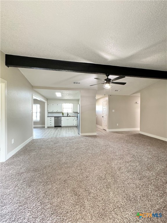 unfurnished living room featuring beamed ceiling, sink, ceiling fan, a textured ceiling, and light colored carpet