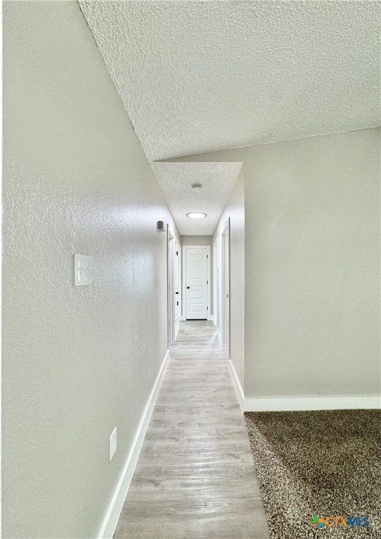 hall with a textured ceiling and light wood-type flooring